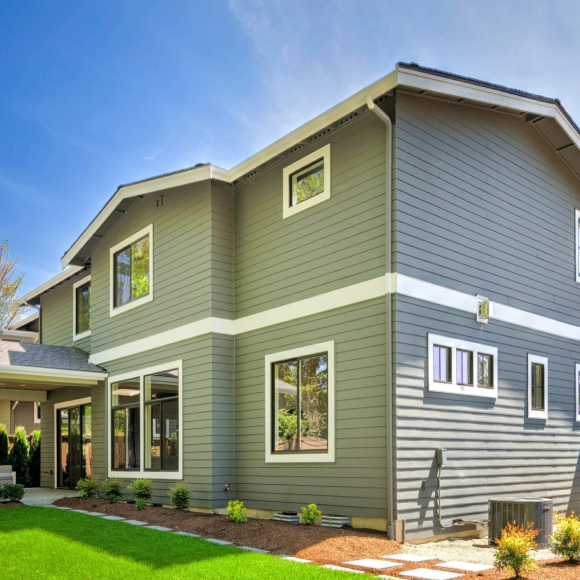 modern two-story house with grey siding and large windows in a landscaped yard