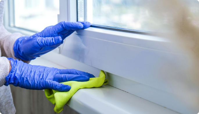 person cleaning window frame with cloth and gloves