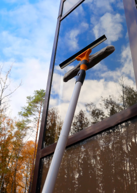 window cleaning with squeegee on tall glass building reflecting sky and trees