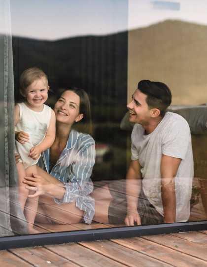 family smiling through a clean large glass window with a baby in the mother's lap