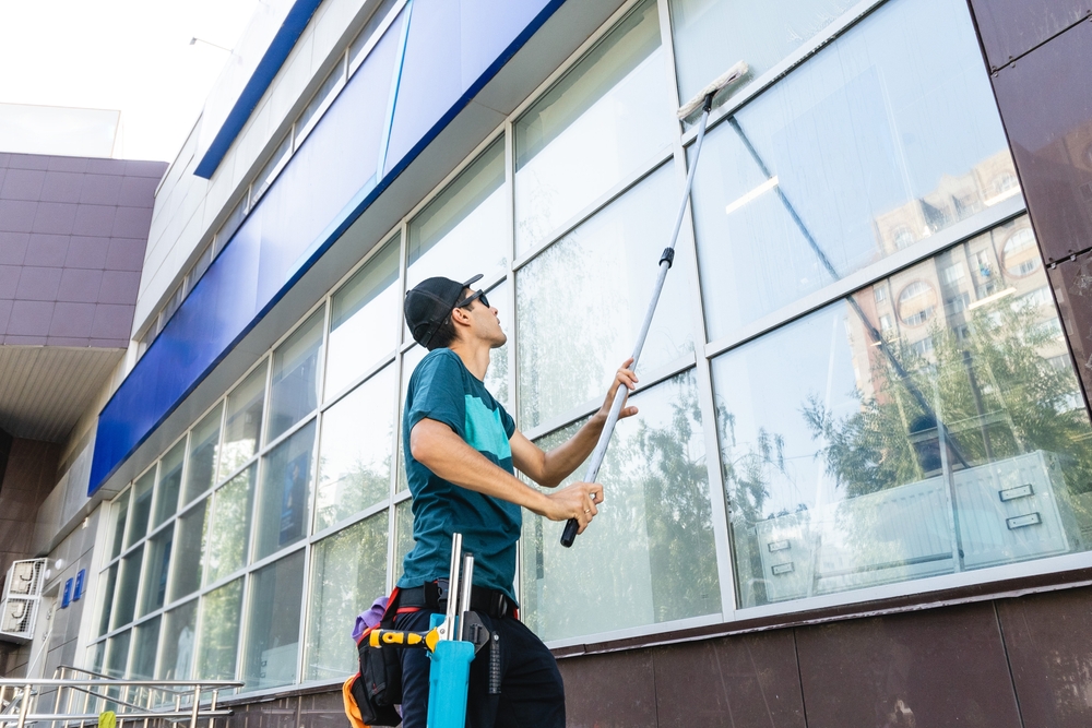 worker cleaning large glass windows of a commercial building with a squeegee on an extended pole