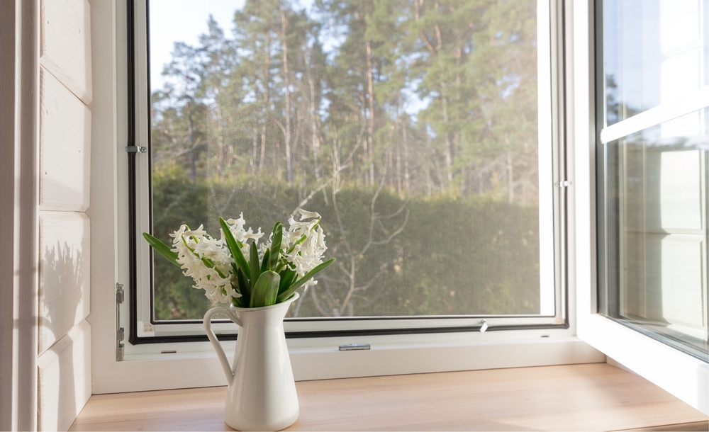 open window with a vase of flowers on the windowsill, showing a clear view of trees outside