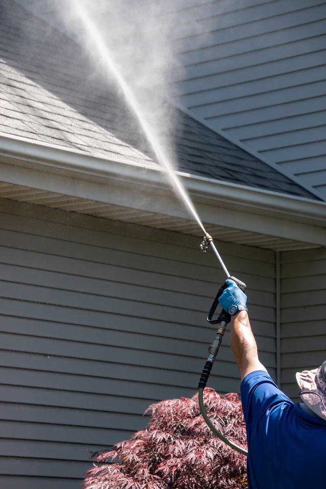 worker pressure washing the exterior of a house near the roofline