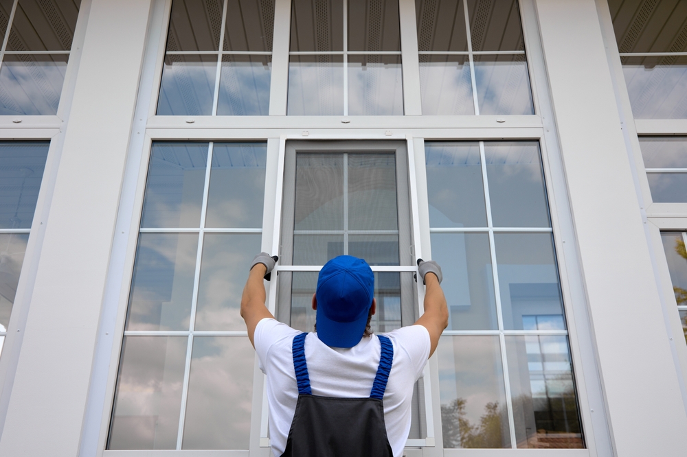 worker installing a window screen on a large glass window