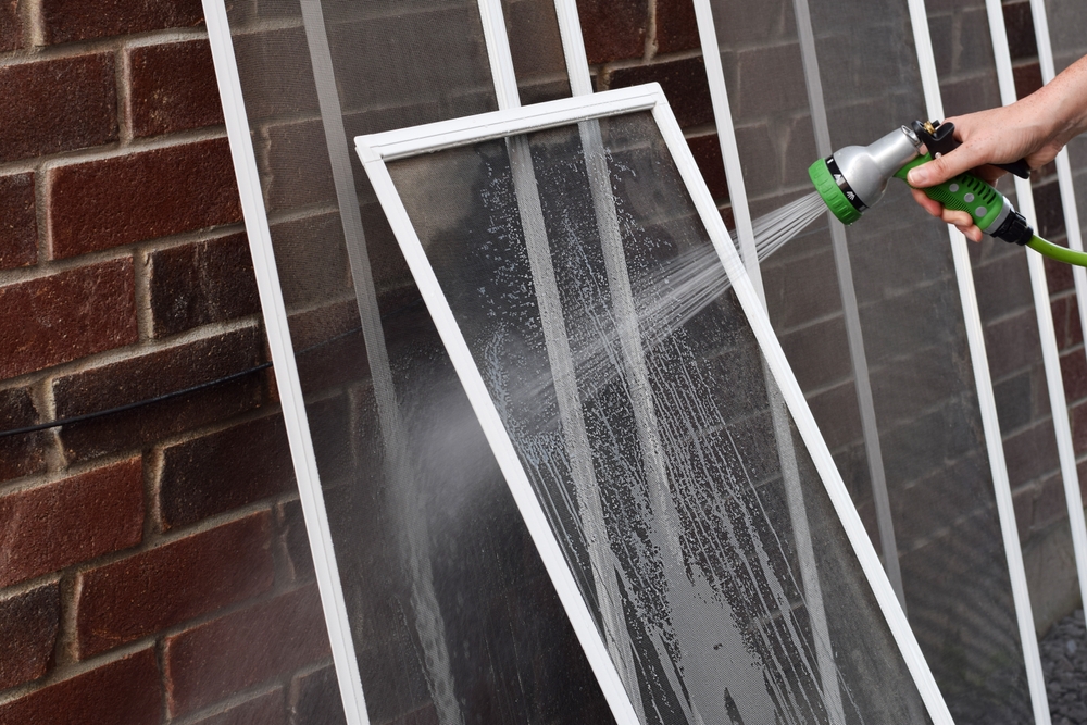 person spraying a window screen with a garden hose