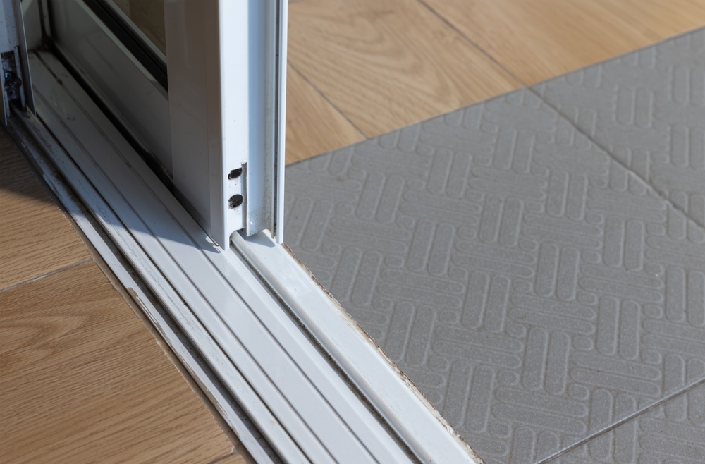 dirty sliding door track on a tiled and wooden floor